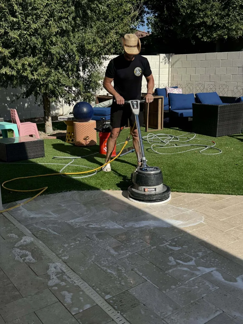 Pavers being scrubbed clean right next to the artificial turf in a backyard