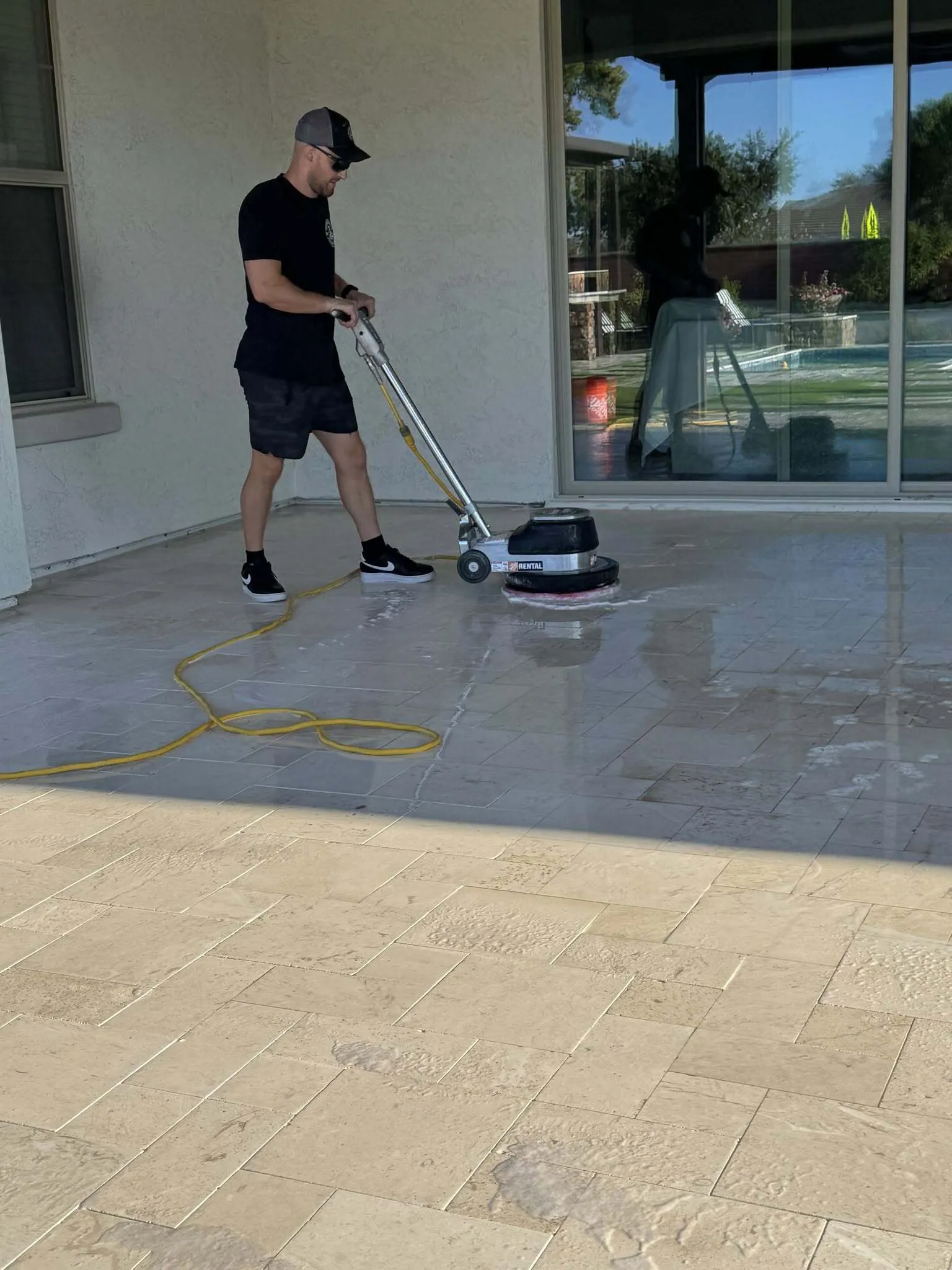 Technician using a commercial floor buffer to deep clean a covered travertine patio before sealing