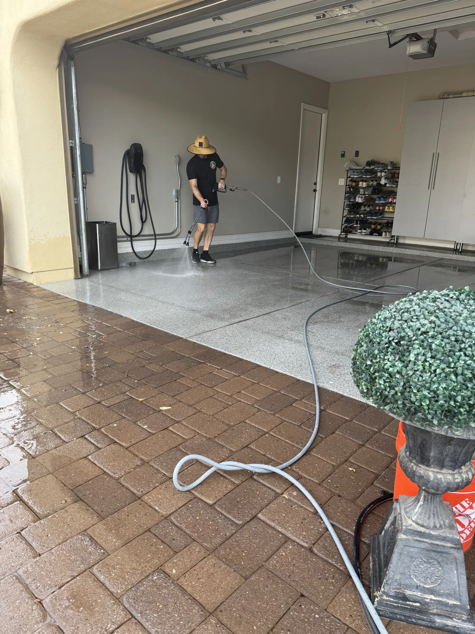 Technician pressure washing an epoxy garage floor beyond a wet brick paver driveway