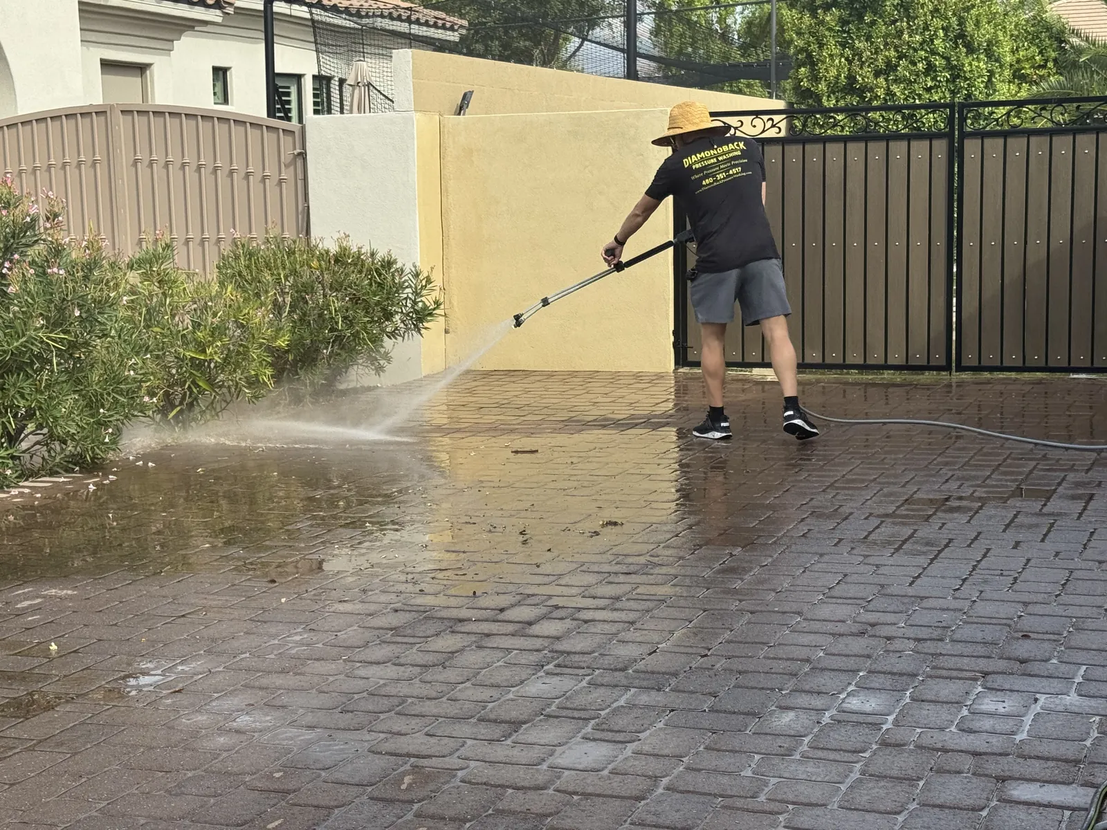 Technician sweeping pressure-washer spray to push dirt off brick pavers toward a planter