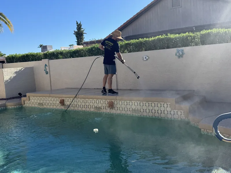 Technician pressure washing a raised concrete ledge beside a backyard pool