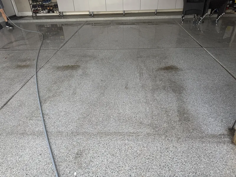 Dark tire stains on a speckled garage floor, with the freshly rinsed section behind