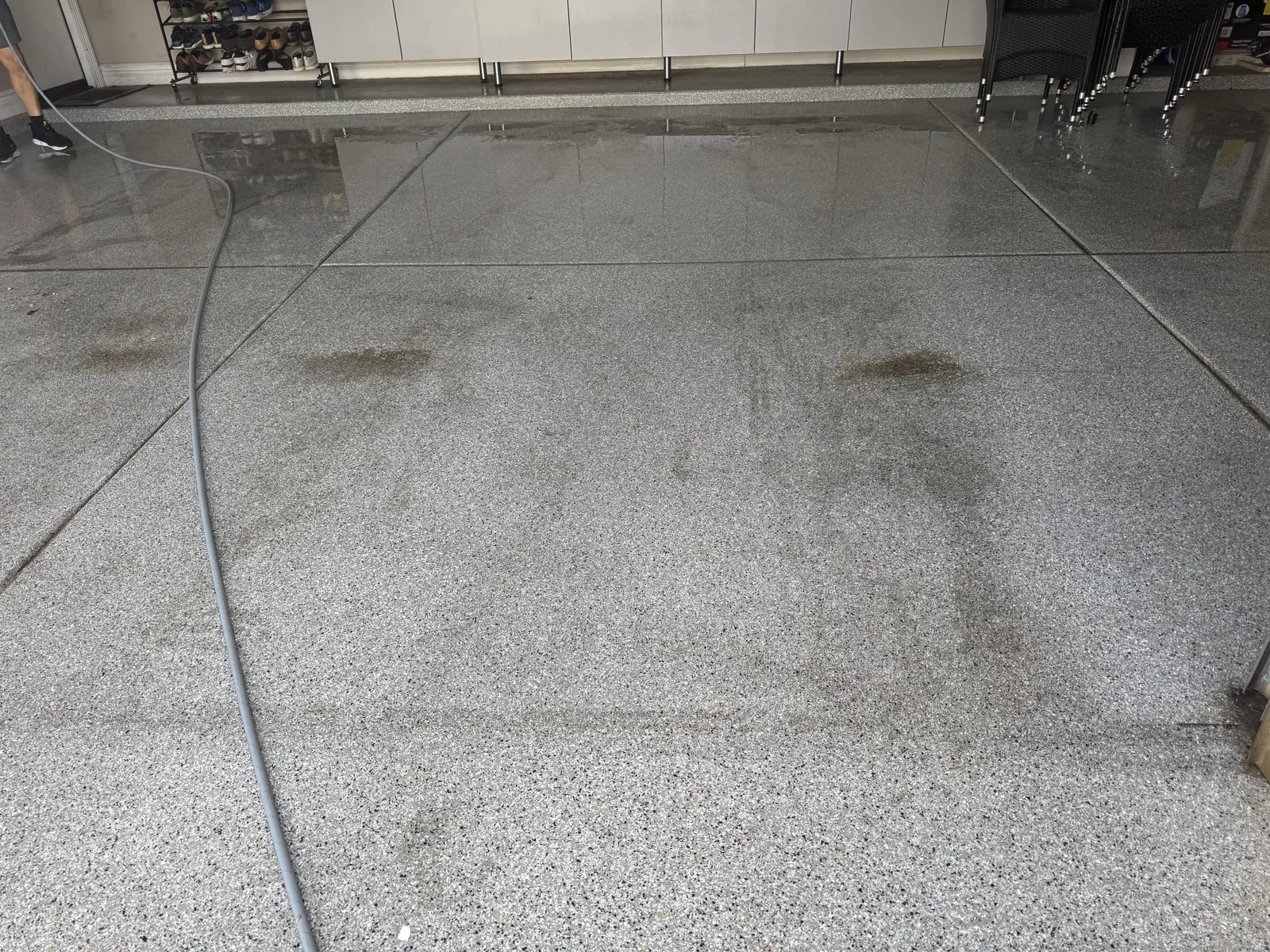 Speckled garage floor mid-cleaning: tire stains in front, rinsed glossy section behind
