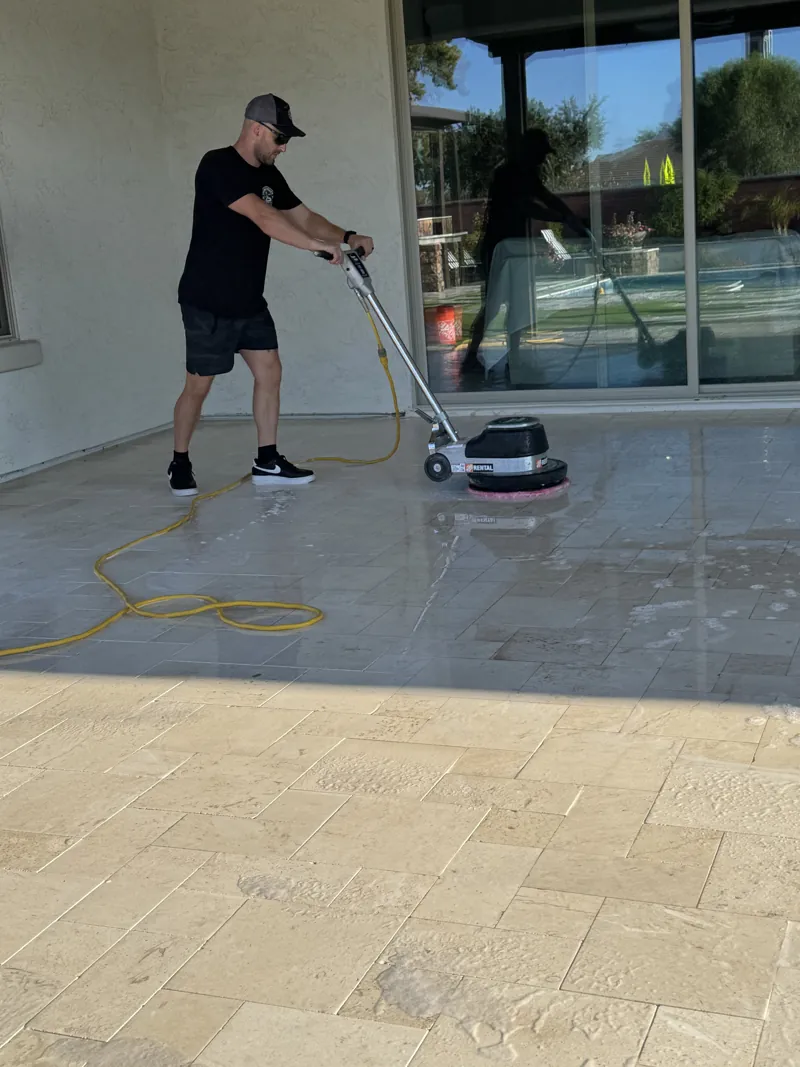 Technician buffing a covered travertine patio, the cleaned stone still wet beside dry stone